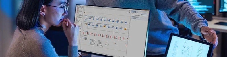 Two people analyzing a computer simulation model displayed across multiple screens in an office setting